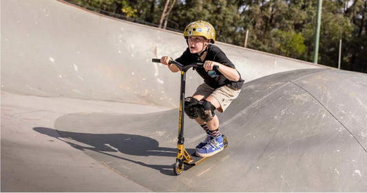 Young rider in helmet and knee pads on a freestyle scooter at a skatepark